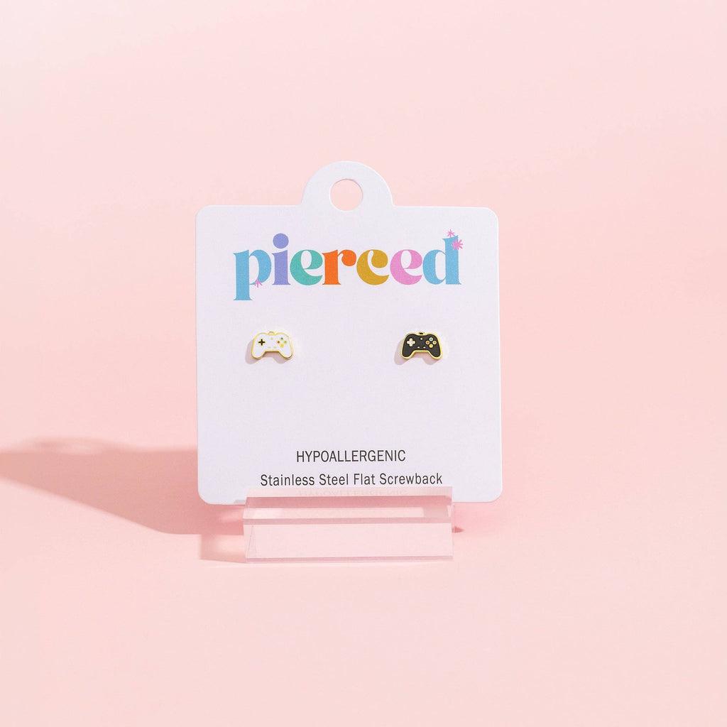 A pair of small stainless steel flatback screwback earrings displayed on a white Pierced brand card, set against a solid pastel pink background.