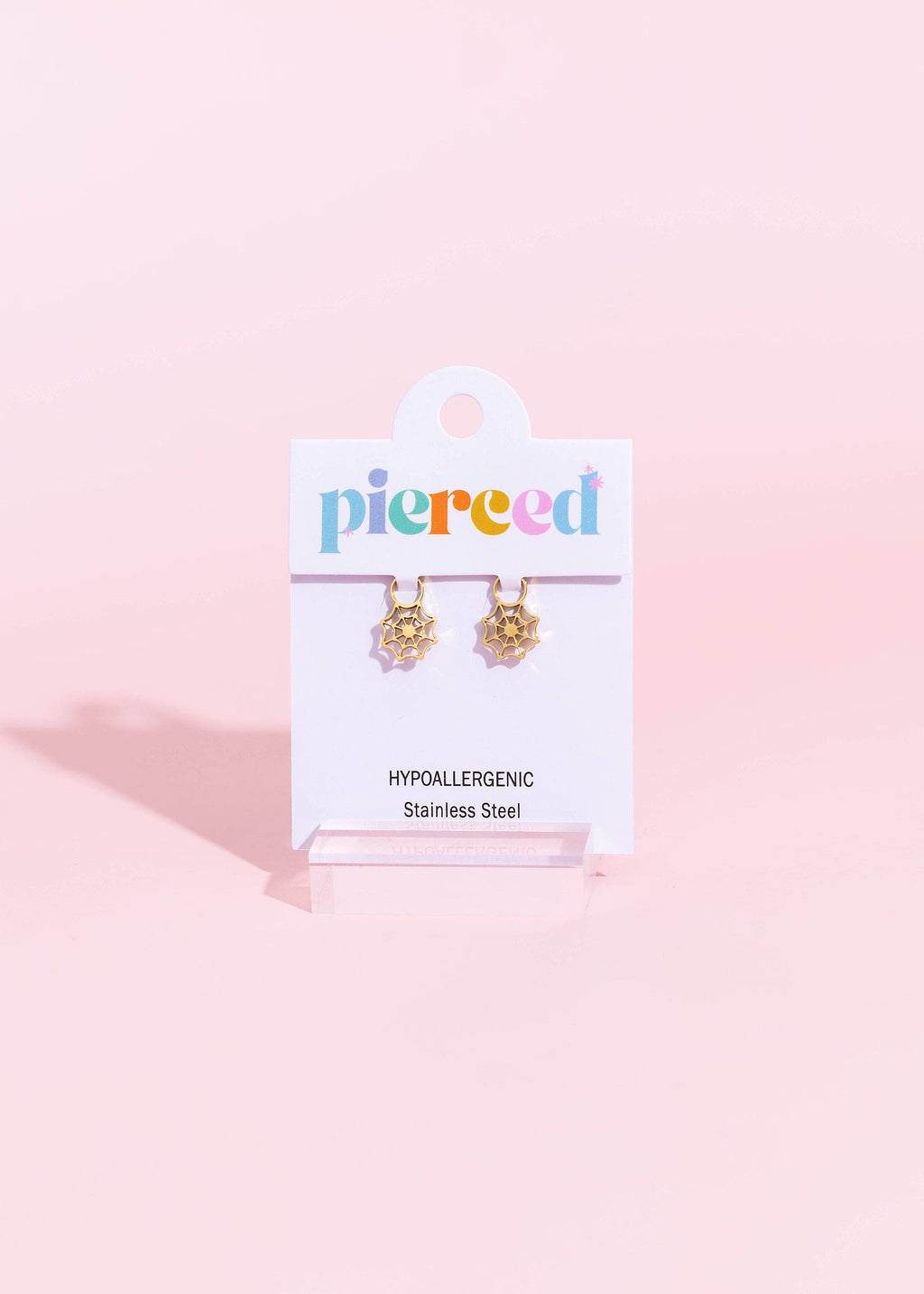 A pair of gold-toned dangle earrings displayed on a white Piered brand card, set against a solid pastel pink background.
