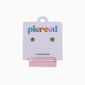 Two small gold star-shaped stud earrings displayed on a white card labeled 'pierced' with a pink stand against a light gray background.