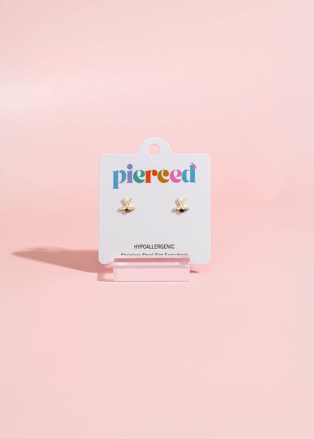 A pair of small gold butterfly stud earrings on a white Pierced brand display card, set against a soft pink background.