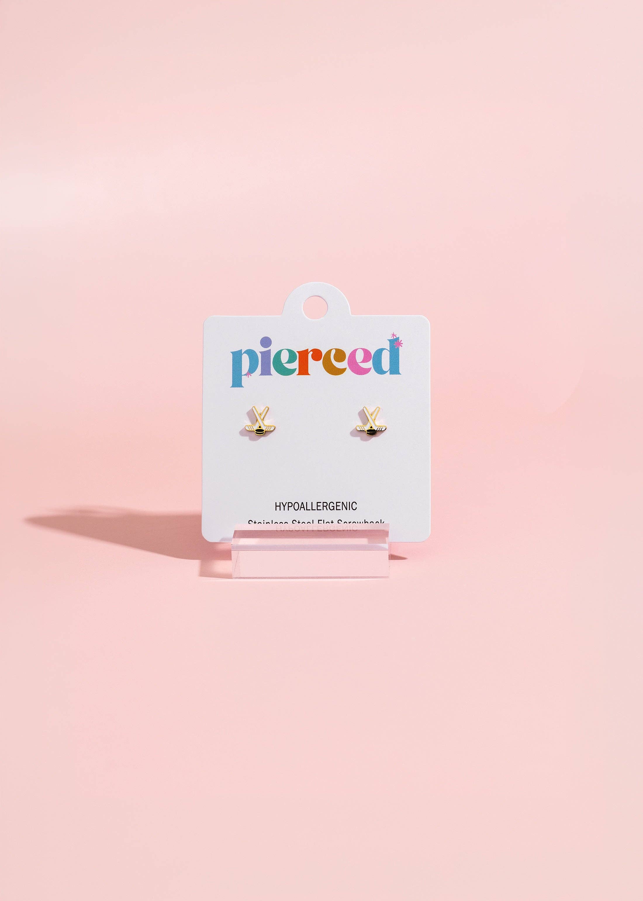 A pair of small gold butterfly stud earrings on a white Pierced brand display card, set against a soft pink background.