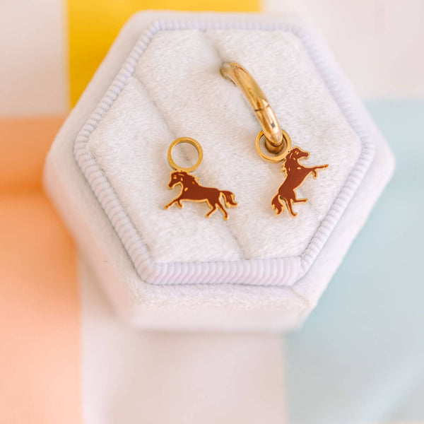 Gold horse-shaped earrings in a hexagonal jewelry box with a soft background