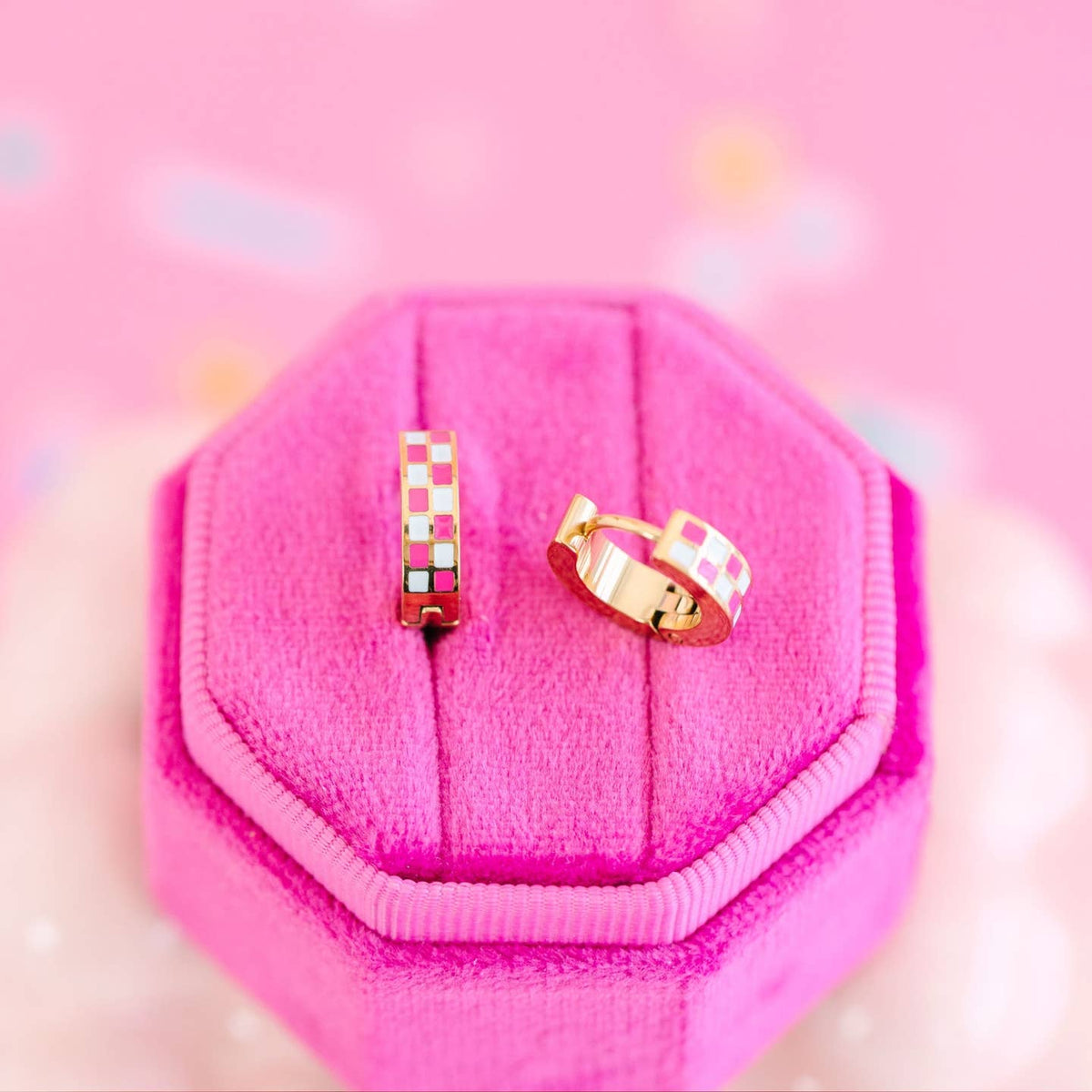 Two gold rings with pink gemstones on a pink jewelry box.