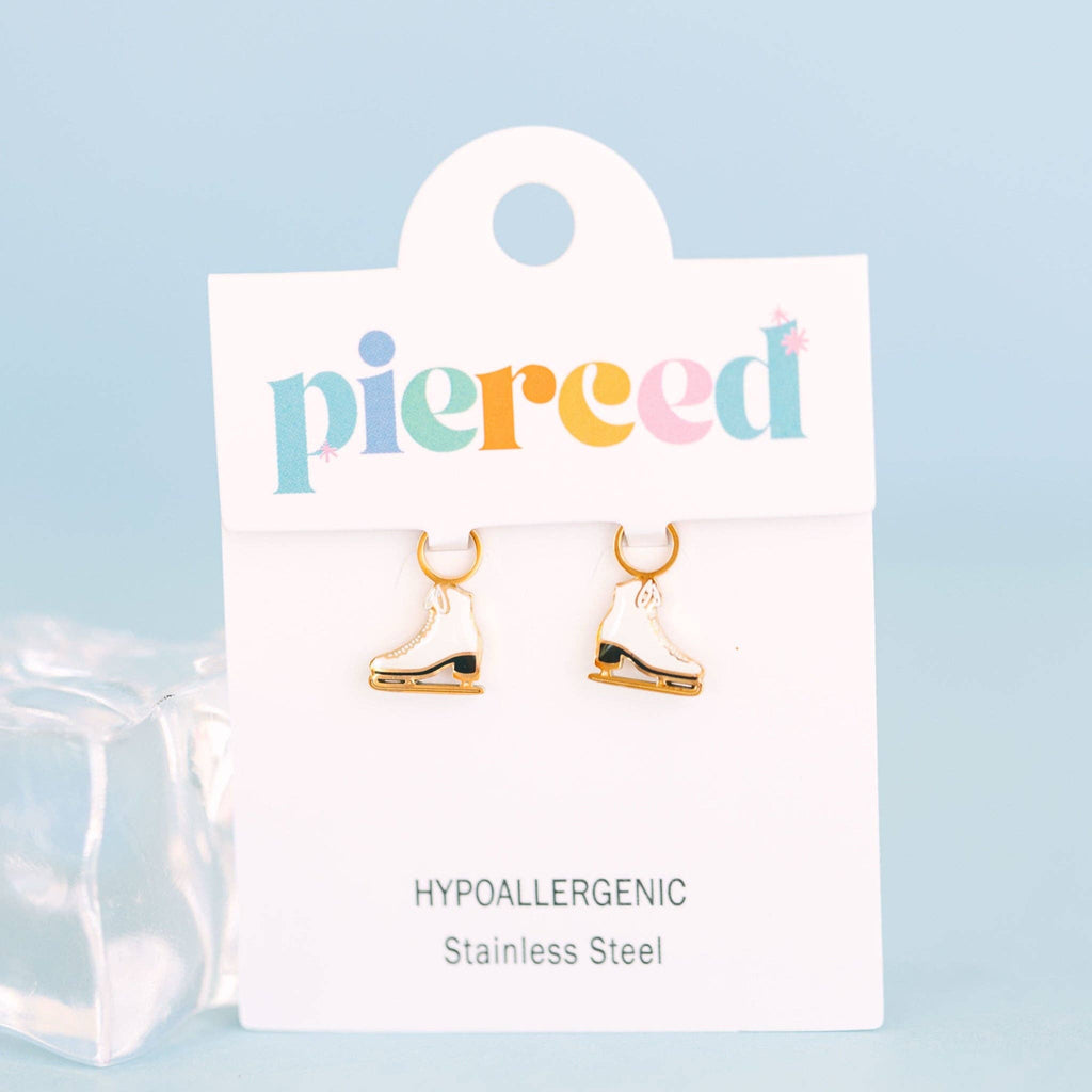 A pair of small ice skate earring charms displayed on a white jewelry card. The card has the word 'pierced' in multicolored letters at the top and reads 'HYPOALLERGGENic Stainless Steel' at the bottom.