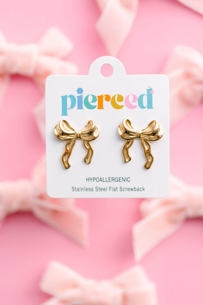 Gold bow-shaped earrings on a 'pierced' branded card against a pink background