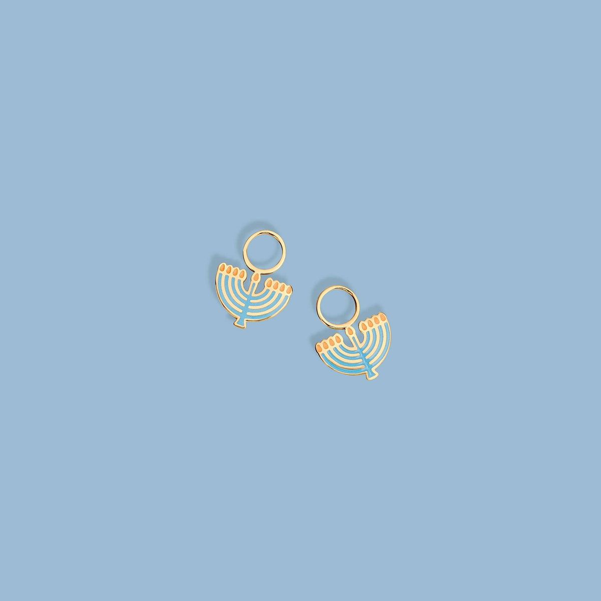 A pair of gold-tone menorah-shaped earrings with light blue and orange enamel details, displayed on a solid light blue background.