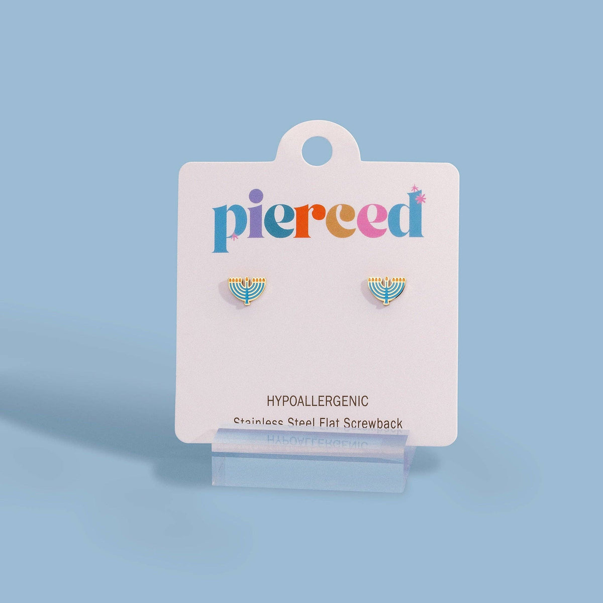 A pair of small gold-tone and teal enamel stud earrings displayed on a white card labeled 'pierced' against a light blue background.