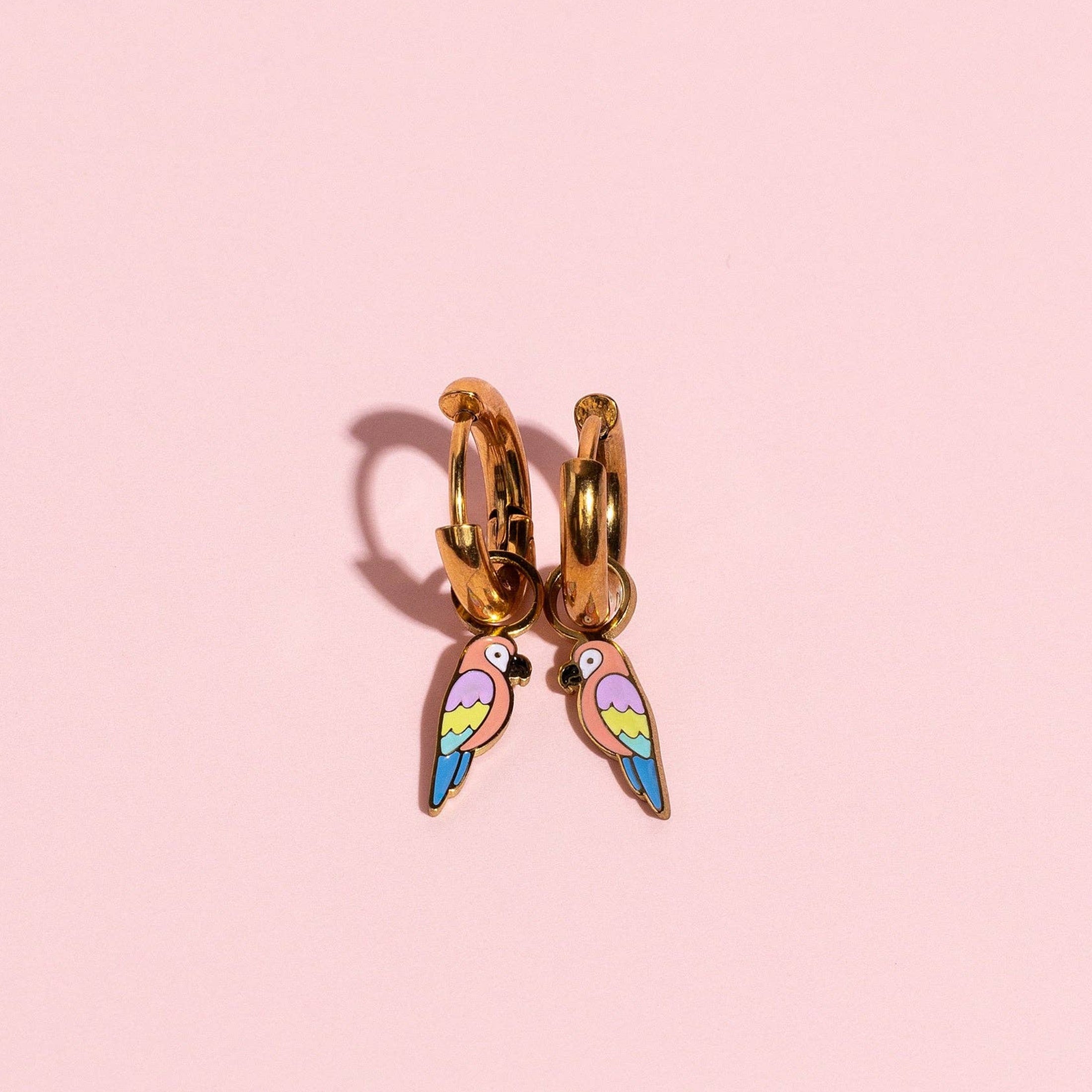 Gold hoop earring with colorful wing design on a pink background