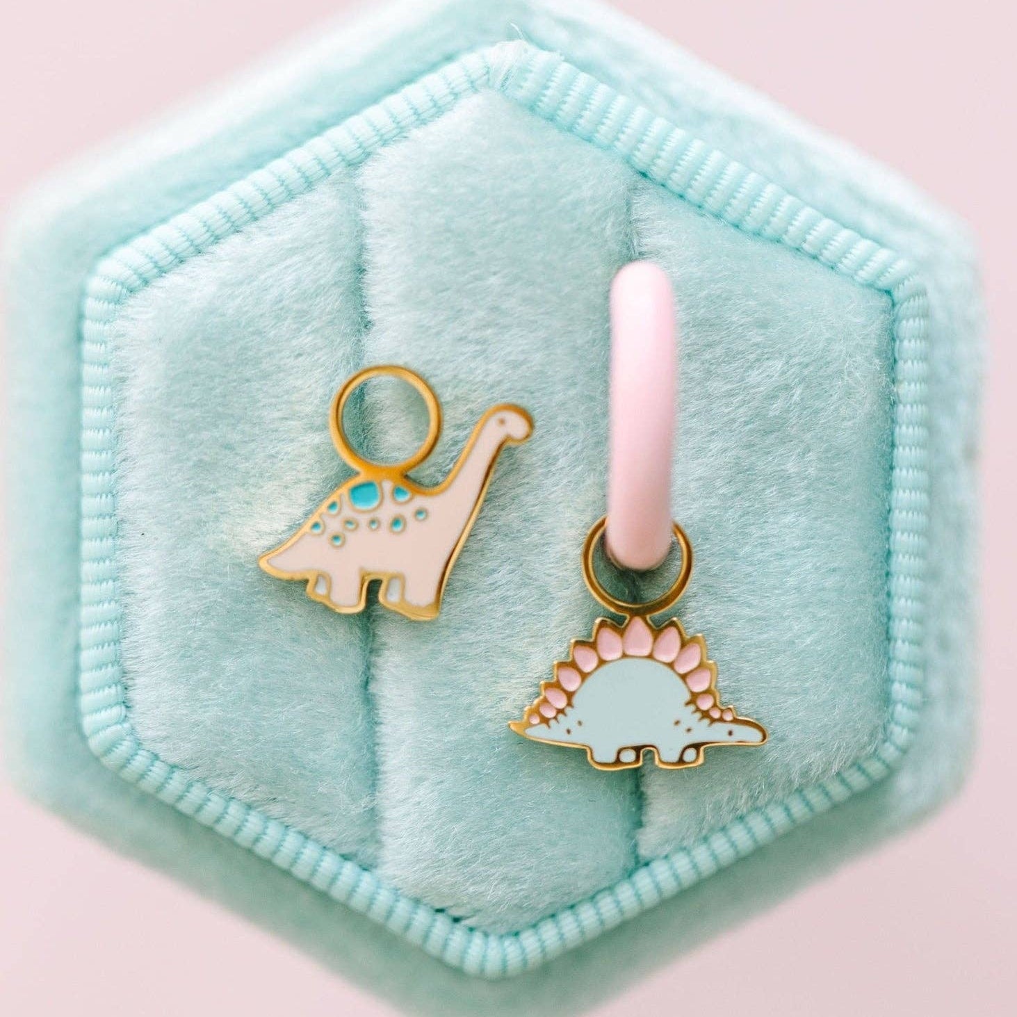 Two dinosaur-shaped charms on a pink background