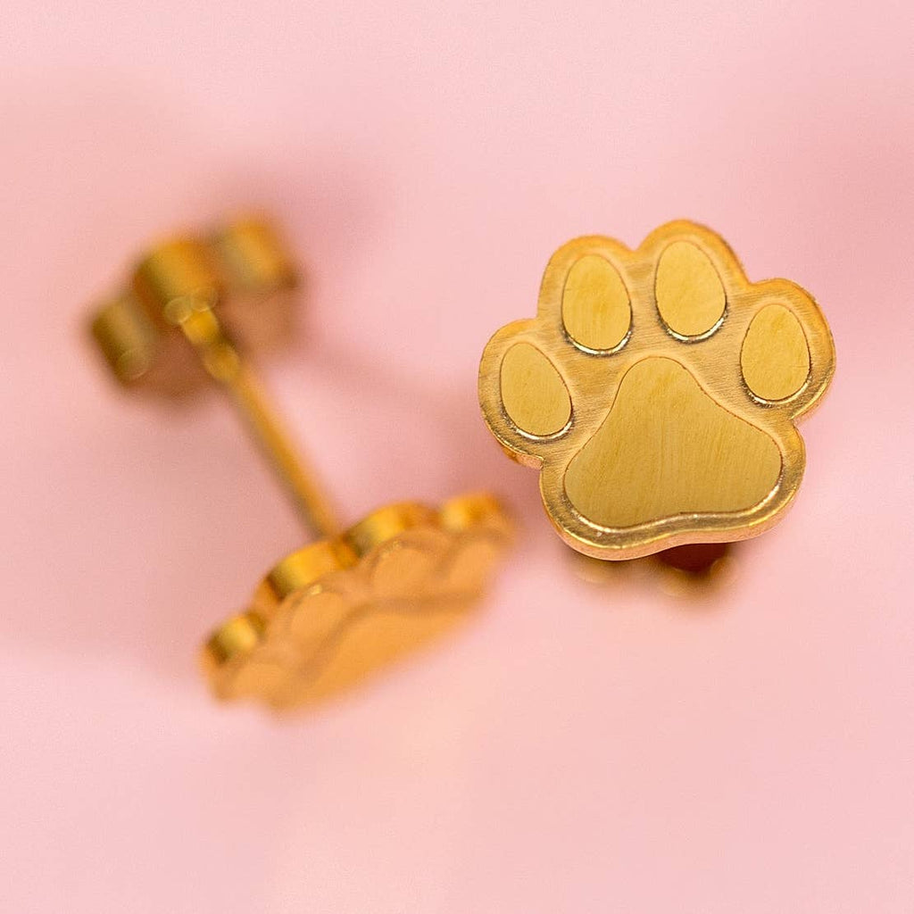 Gold paw print earrings on a pink background