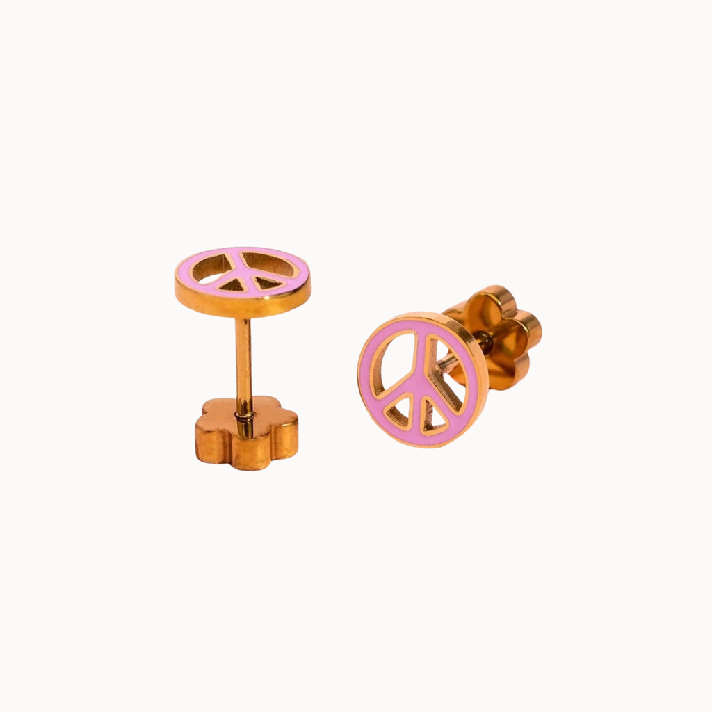 A pair of gold-plated peace sign stud earrings with a pink enamel center, displayed on a clean off-white background.