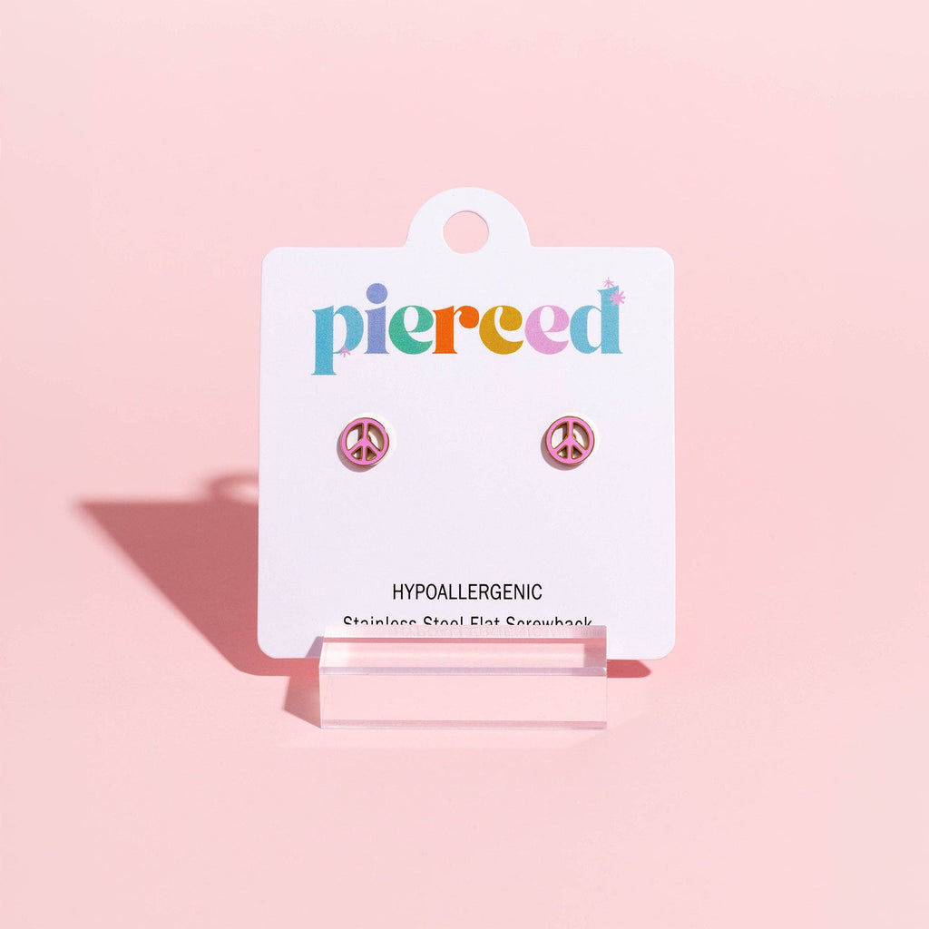 A pair of small stud earrings displayed on a white Pierced brand card, set against a solid pastel pink background.