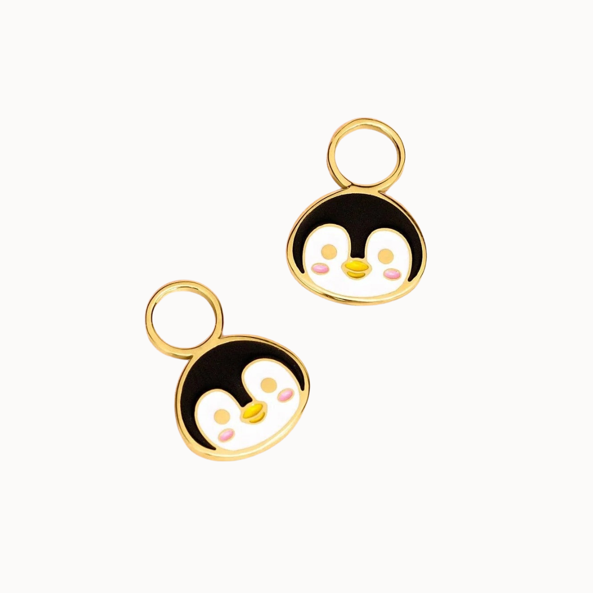 Two gold penguin-shaped charms with black, white, yellow, and pink enamel details, displayed on a clean white background.
