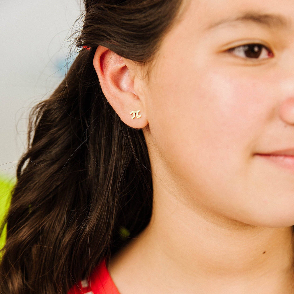 A close-up of a person wearing a small gold double-C stud earring, with long dark brown hair and a red and white striped top.