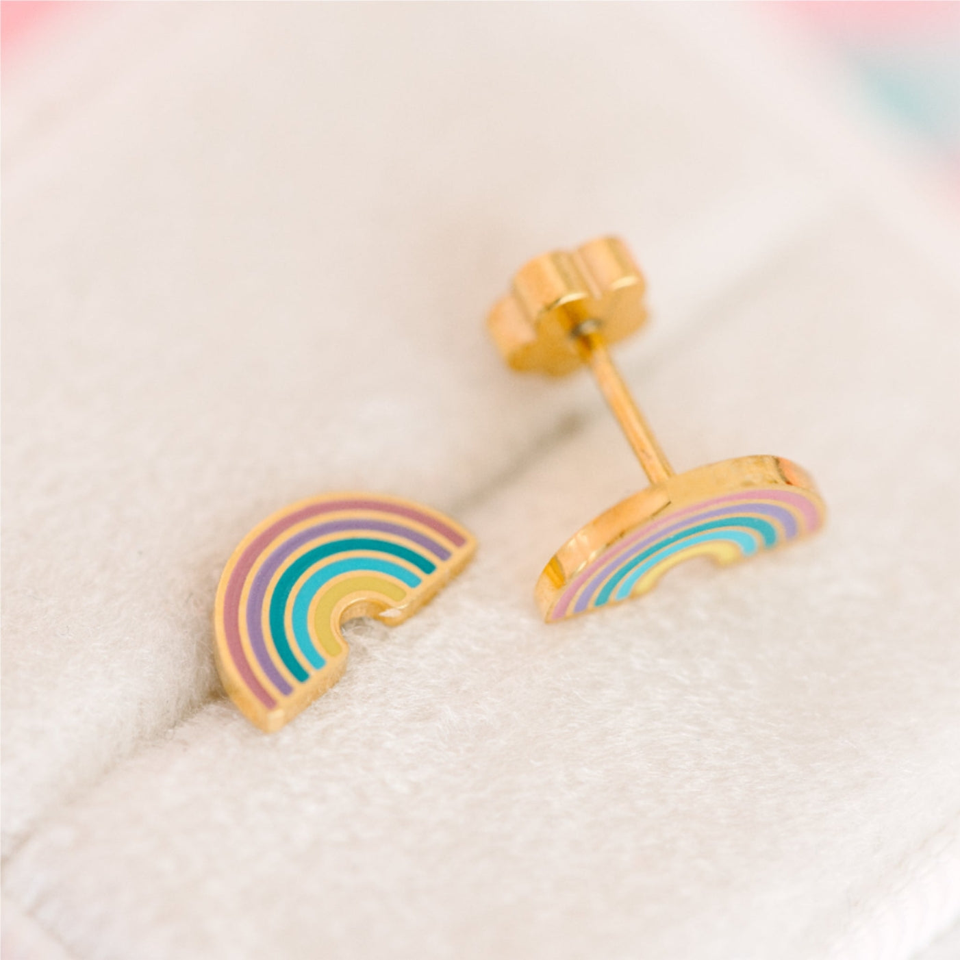 Rainbow-shaped earrings on a soft fabric background
