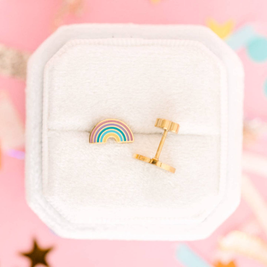 Rainbow-shaped earrings in a white jewelry box on a pink background with star decorations.