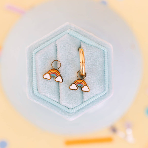 Rainbow-shaped earrings in a hexagonal jewelry box with a light blue interior.