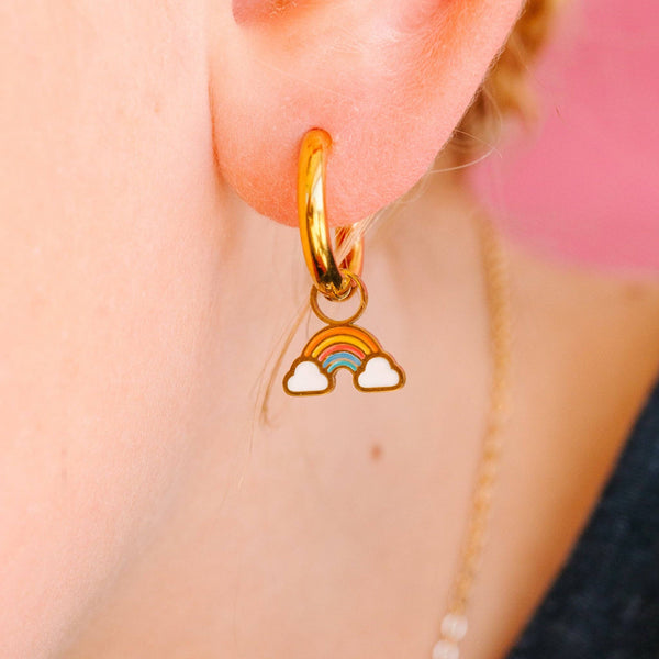 Gold hoop earring with a rainbow charm worn by a person.