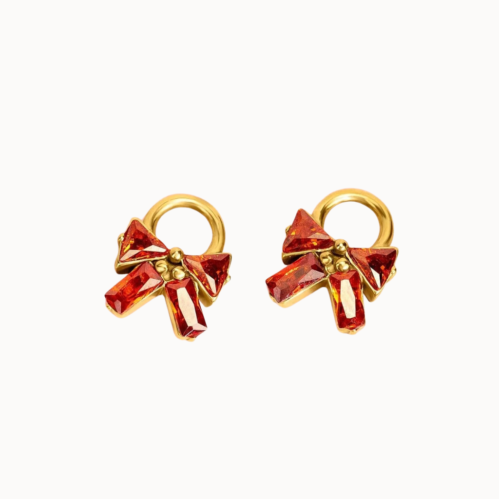 A pair of gold hoop earrings featuring a faceted red crystal bow with a small gold bead at the center, set against a plain white background.