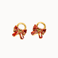A pair of gold hoop earrings featuring a faceted red crystal bow with a small gold bead at the center, set against a plain white background.