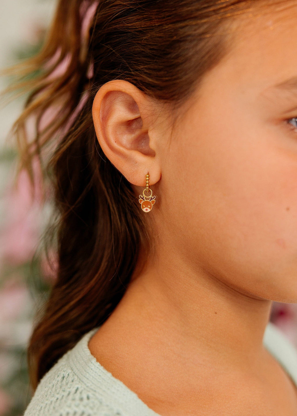 A close-up side profile of a person wearing a small gold hoop earring with a dangling skull charm.