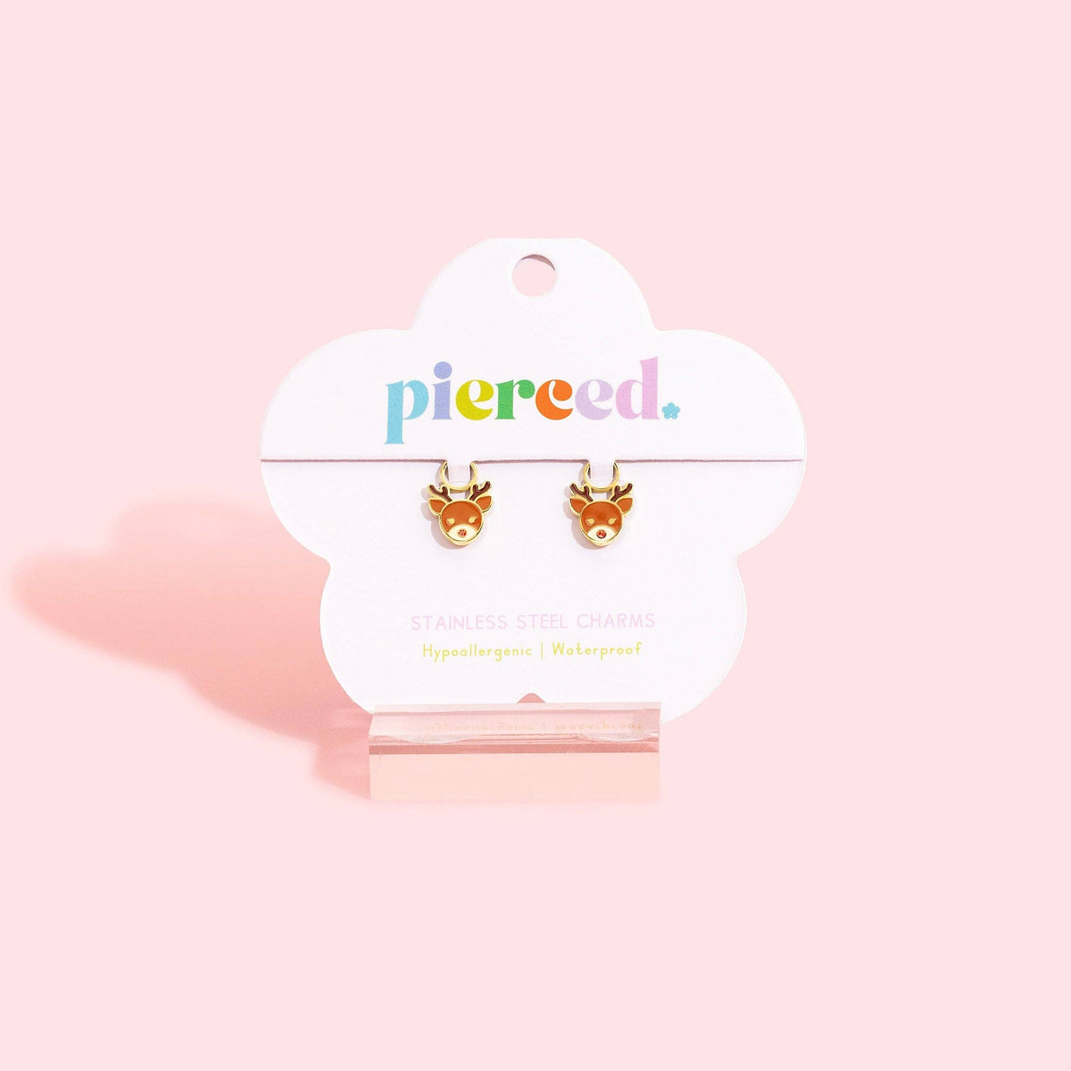 A pair of small deer stud earrings displayed on a white cloud-shaped card labeled 'pierced.' against a soft pink background.