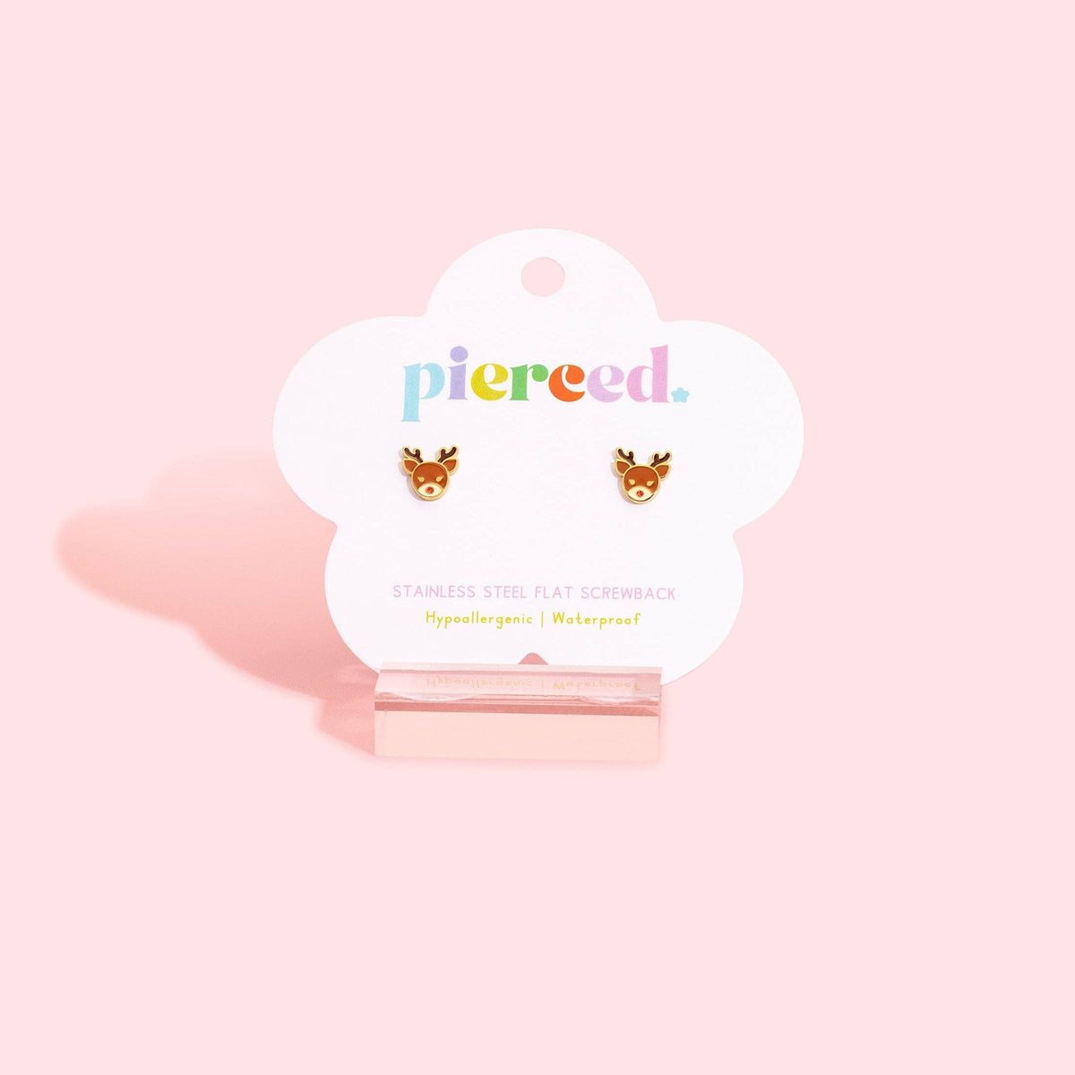 A pair of small deer head stud earrings displayed on a white cloud-shaped card that reads 'pierced.' against a soft pink background.