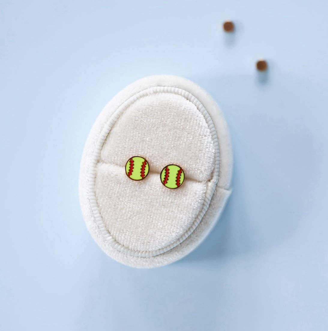 Pair of softball-themed earrings on a white cushion against a light blue background