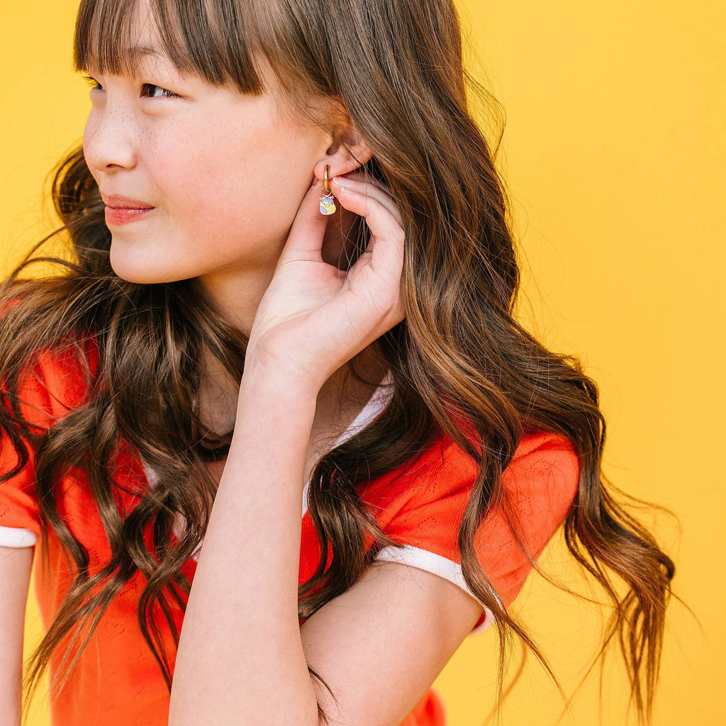Woman adjusting earrings against a yellow background