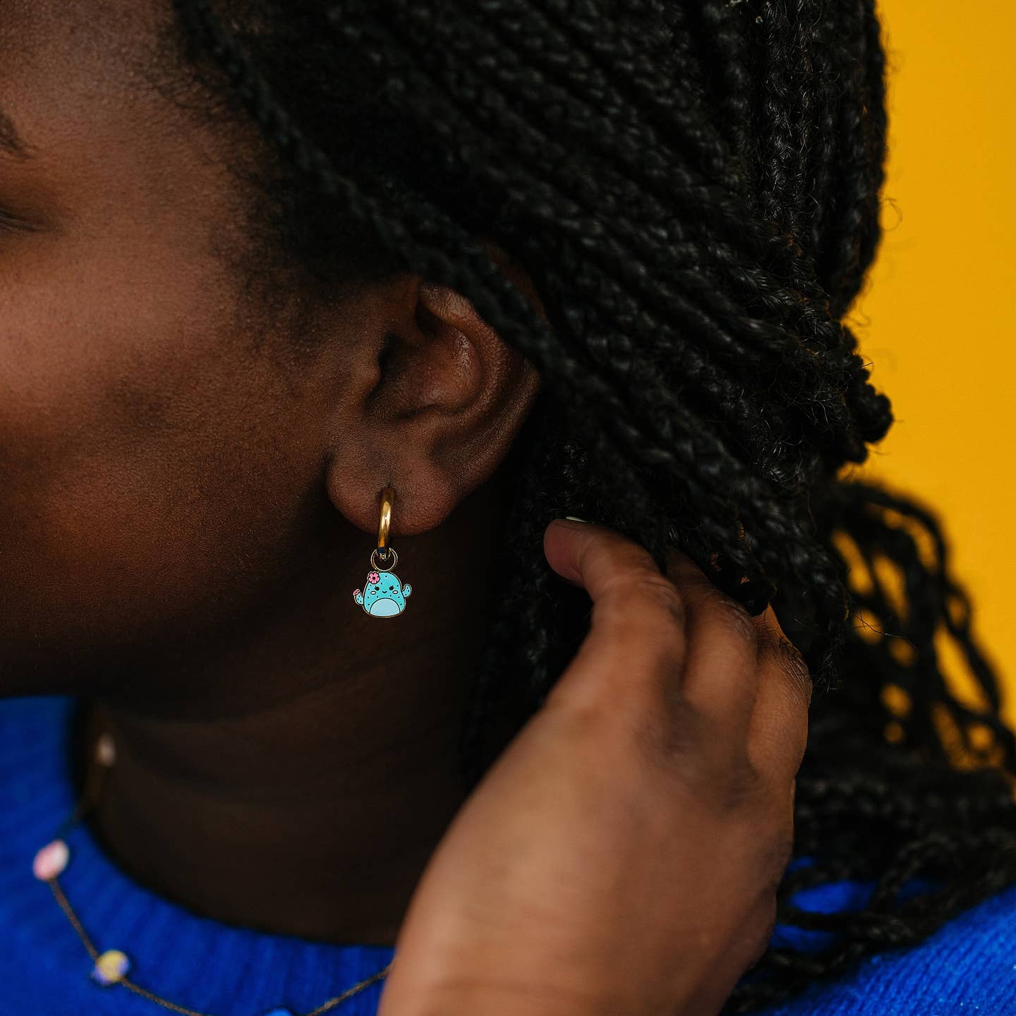 Person wearing a turquoise charm earring with a yellow background
