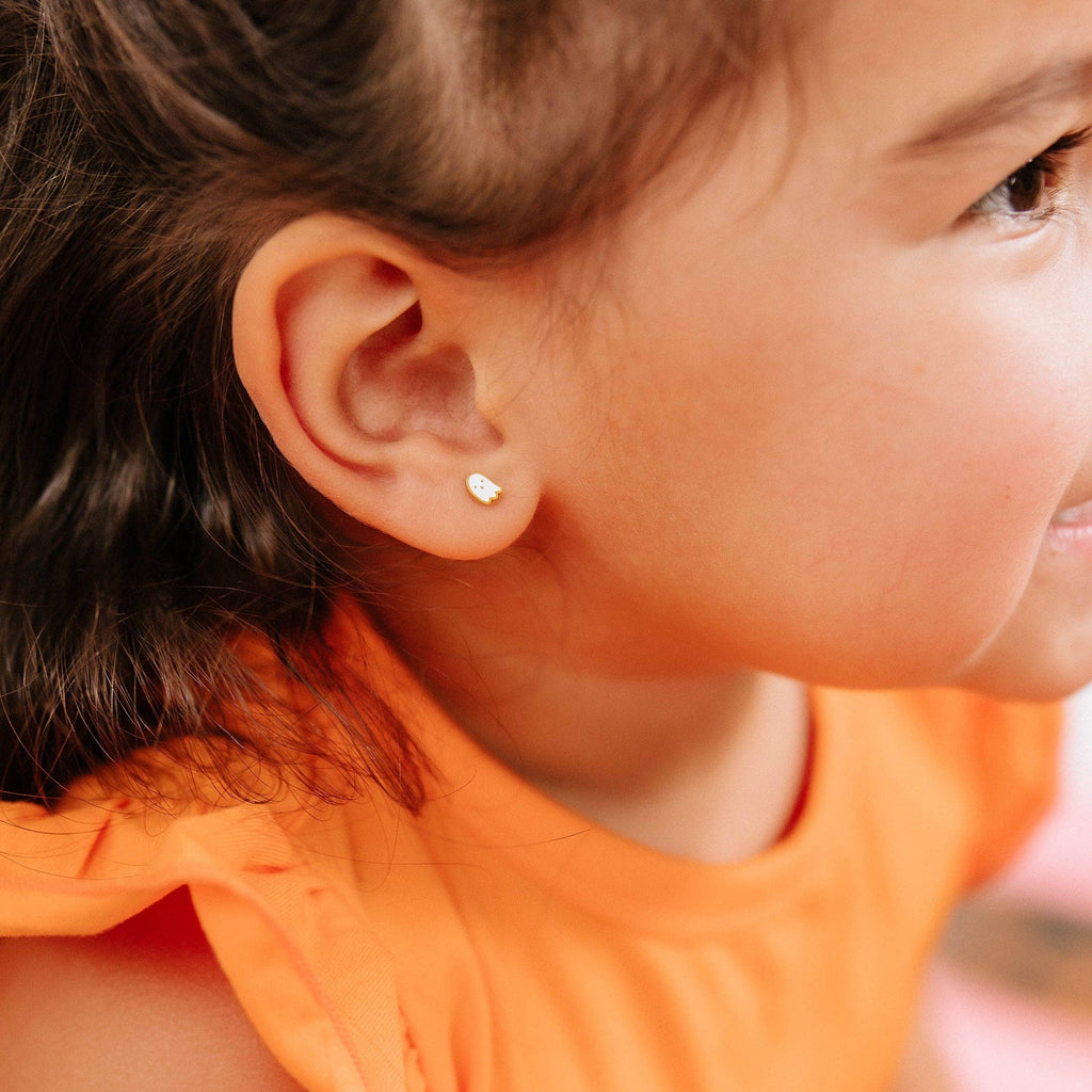 A close-up side profile of a young child wearing a tiny gold heart-shaped stud earring, wearing an orange top.