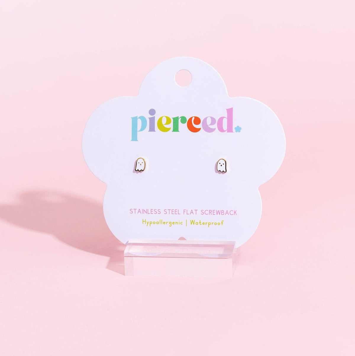 A pair of small flat stainless steel screwback earrings displayed on a white cloud-shaped Pierced brand card, set against a solid pastel pink background.