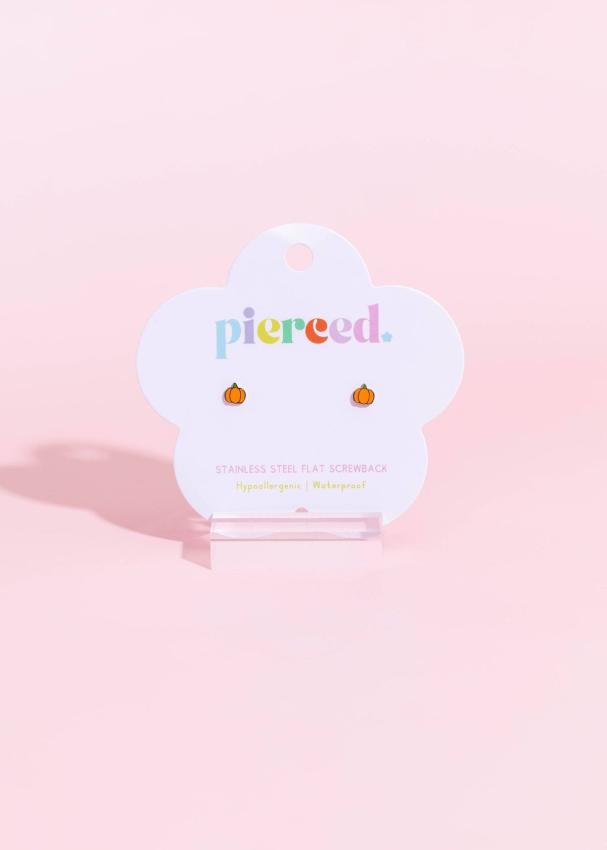 A pair of small pumpkin-shaped stud earrings displayed on a white cloud-shaped card that reads 'pierced.' against a soft pink background.