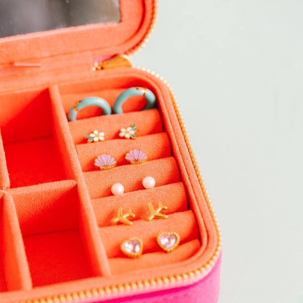 Open pink jewelry case with various earrings on a light gray background