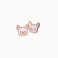 Two small dog-shaped enamel pins on a plain white background. One pin shows a light pink French bulldog face with gold-toned outlines, and the other shows a pale gray French bulldog face with pink inner ears and a gold-toned outline.
