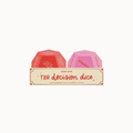 Two TBR decision dice by Pips Post, one red and one pink, displayed in a beige cardboard sleeve on a light gray background.