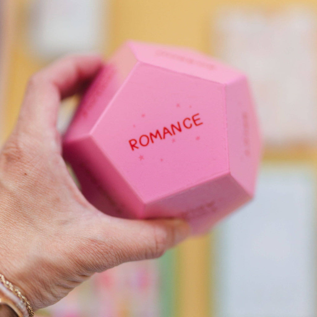 Hand holding a pink dumbbell with 'ROMANCE' written on it against a blurred background