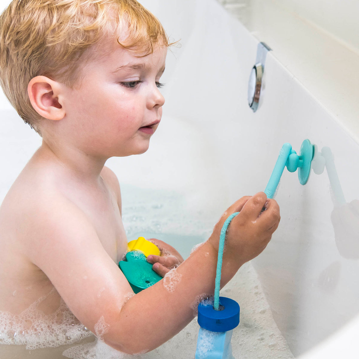 Child playing with a blue toy in a bathtub filled with bubbles