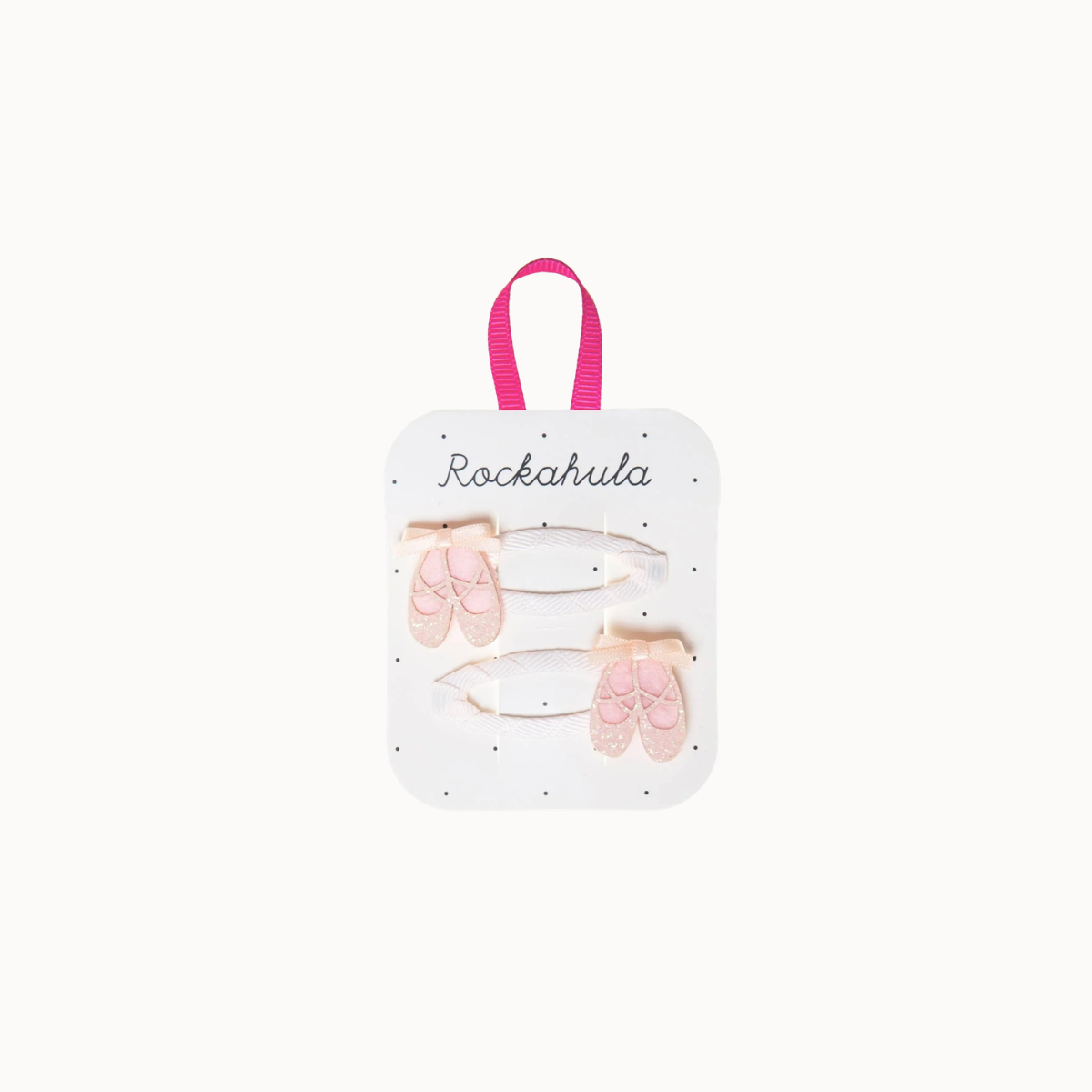 A set of two hair clips shaped like pink ballet slippers, attached to a white display card with a pink handle. The card is branded with the name 'Rockahula' and is photographed against a solid off-white background.