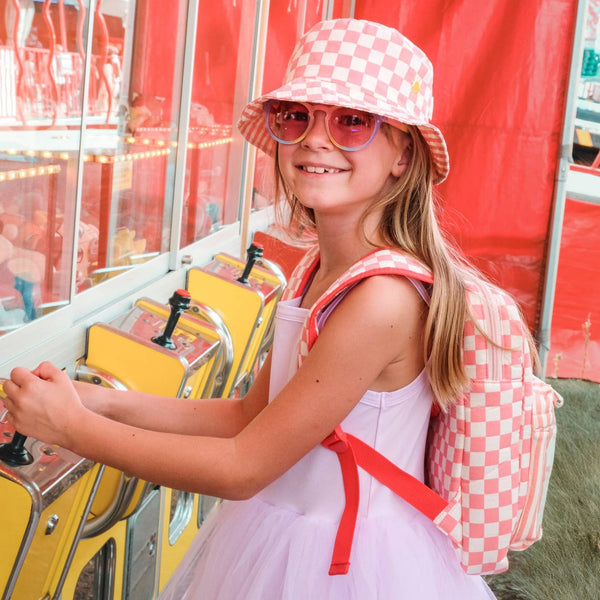 Young girl in a checkered hat and dress playing a carnival game.