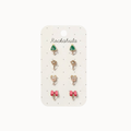 A set of six small stud earrings displayed on a white card labeled 'Rockahula'. The earrings include green Christmas trees, gold stars, pink bows, and teddy bear faces, set in gold-toned metal.