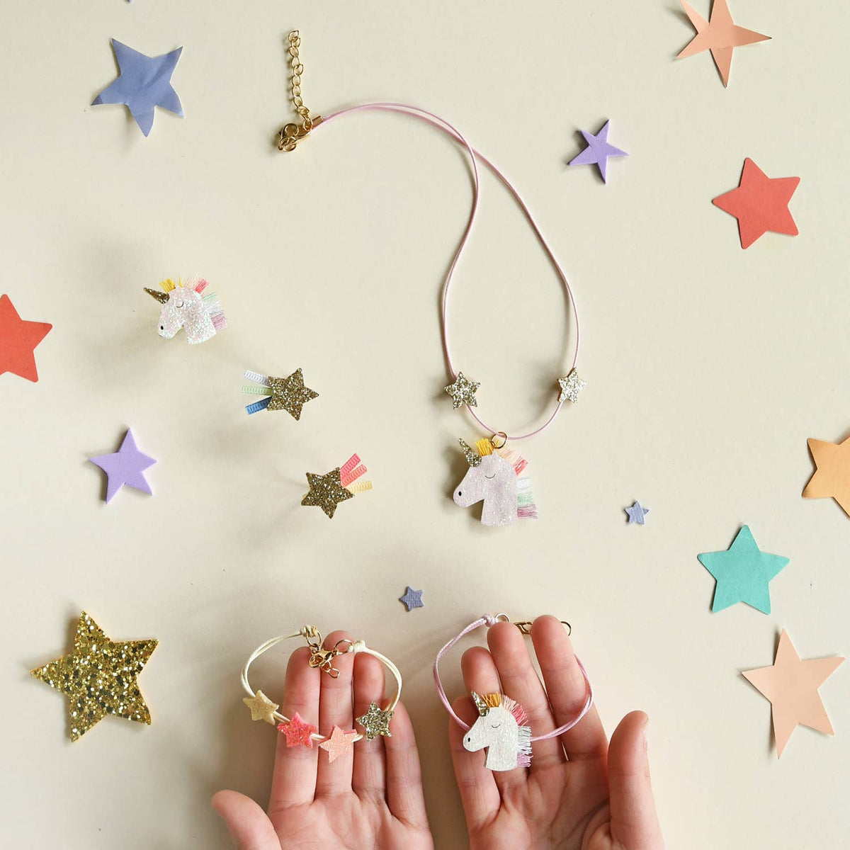 Unicorn-themed jewelry set with necklaces and earrings on a beige background with star decorations.