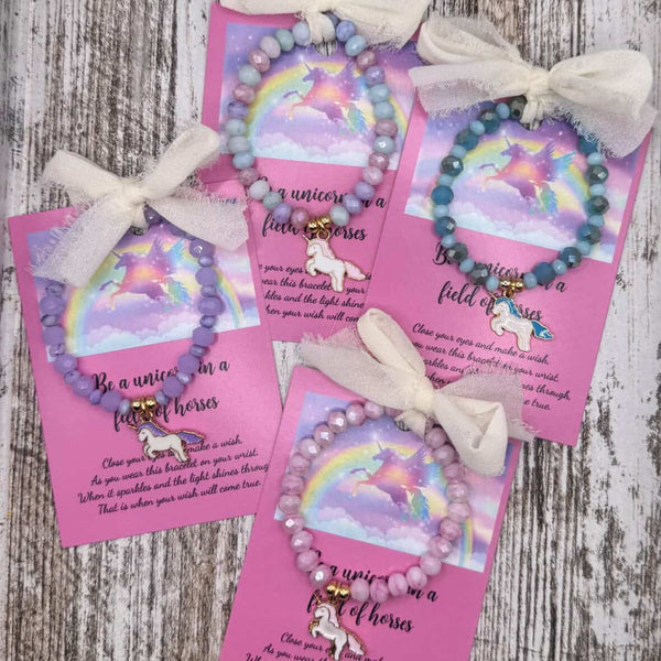 Set of unicorn-themed bracelets with ribbons on pink cards against a wooden background
