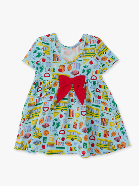 A short-sleeve baby dress with a light blue background and a colorful school-themed print featuring buses, books, apples, and letters. It has a prominent red bow at the center of the chest.