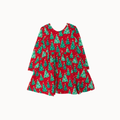 A festive red long-sleeve dress with a green Christmas tree pattern against a white wall with green pine garlands.