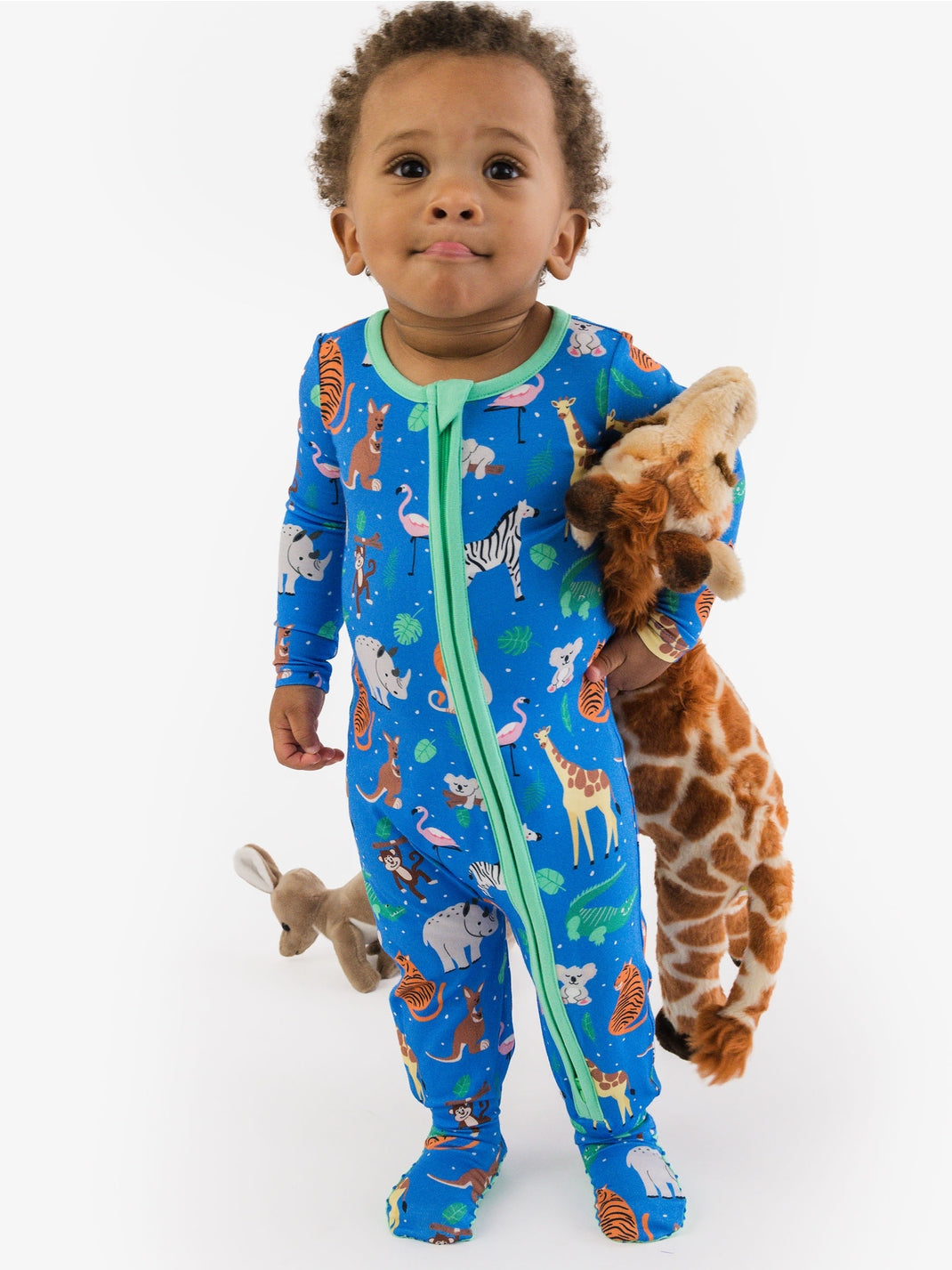 Child wearing a blue animal print onesie holding stuffed giraffe toys on a white background