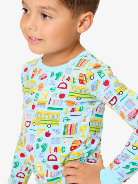 Child wearing a colorful long-sleeve shirt with school-themed patterns on a light blue background