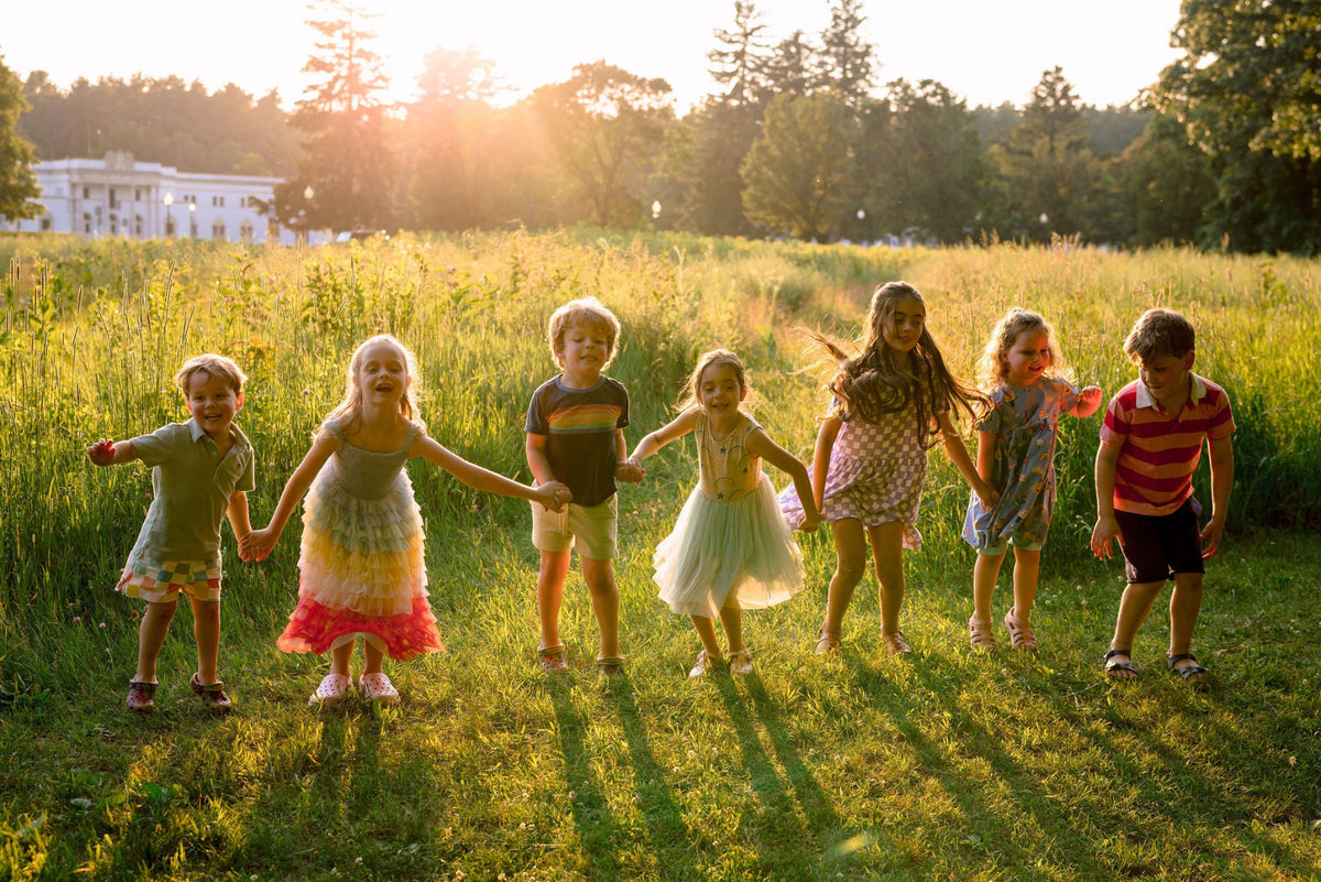 Children holding hands in a field during golden hour sunsent smiling and playing.