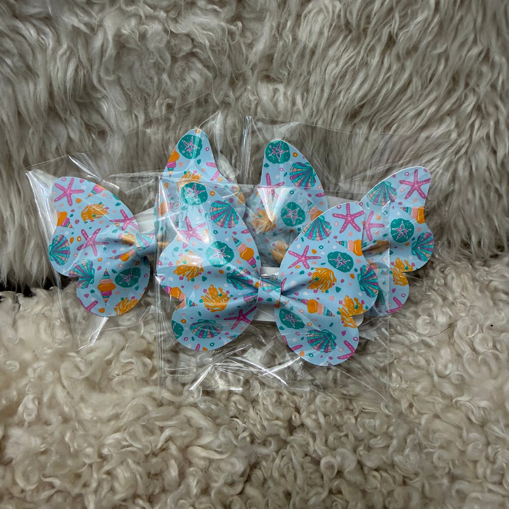 Packaged hair bows with seashell designs on a fluffy surface
