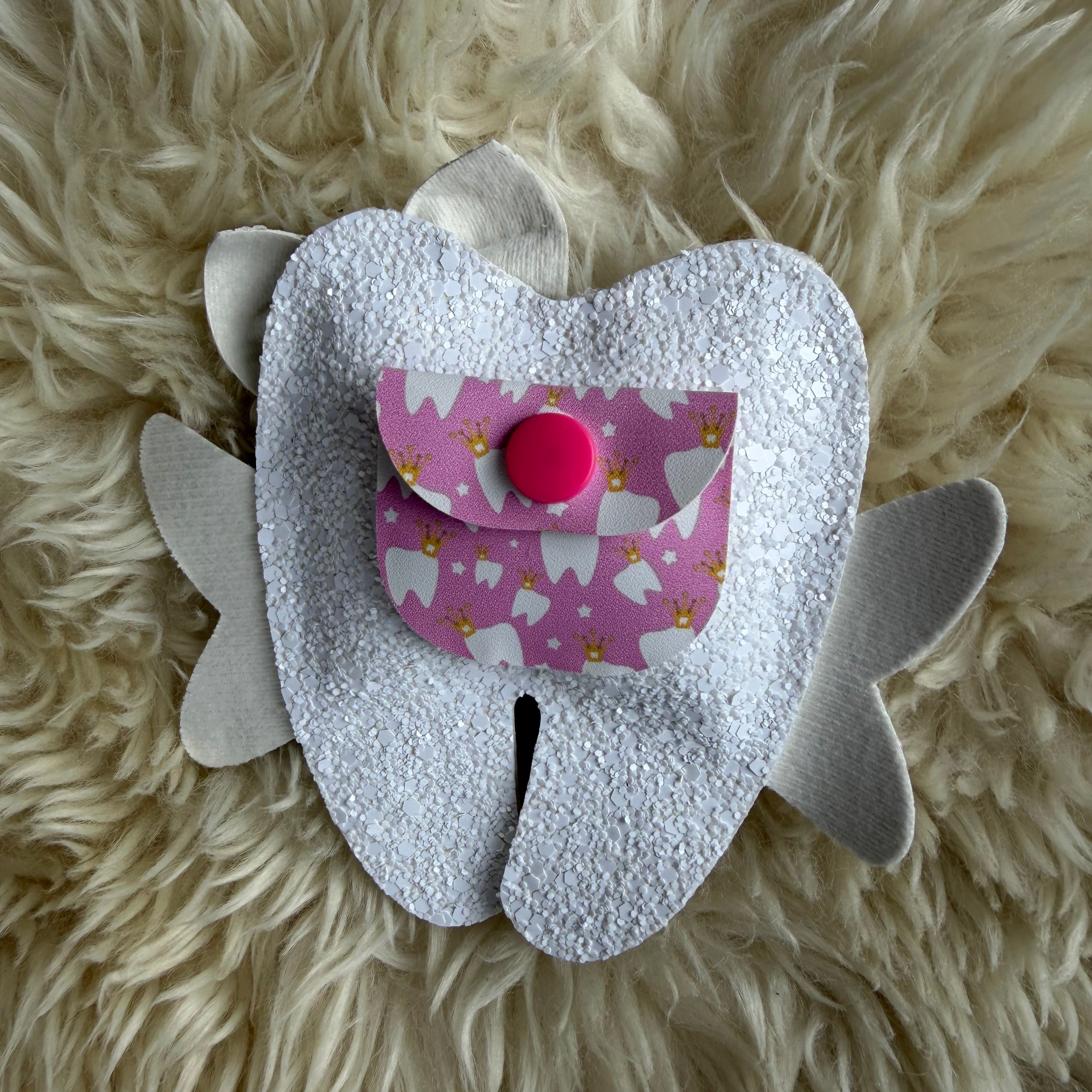 White tooth-shaped pillow with a pink fabric heart on a fluffy white surface